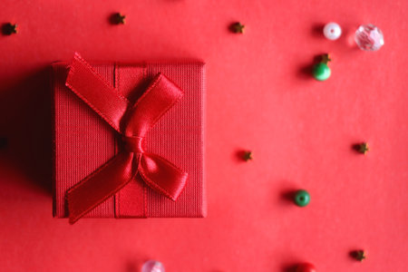 Red present and various beads on red background. Top view.