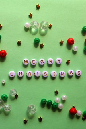 Various beads with Merry Christmas caption on green background. Top view.
