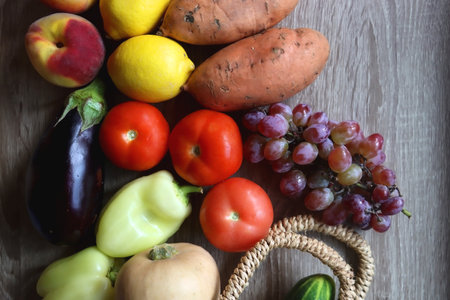 Round straw bag with seasonal fruit and vegetable on wooden background. Late summer or early autumn. Top view.の写真素材