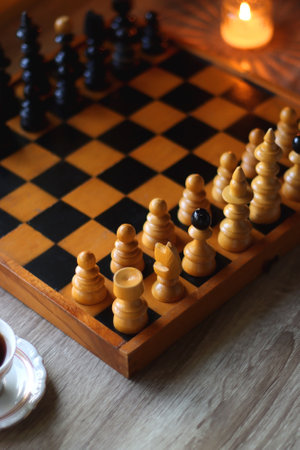 Vintage wooden chessboard, books, glasses, pen, cup of tea or coffee and scented candle on the...