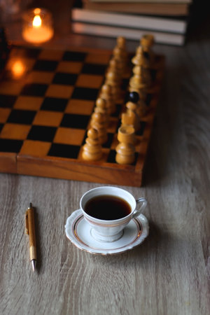 Vintage wooden chessboard, books, glasses, pen, cup of tea or coffee and scented candle on the table. Dark academia concept. Selective focus.の写真素材