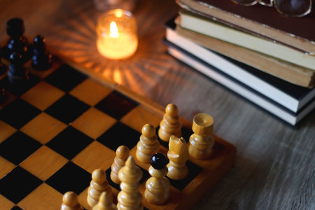Vintage wooden chessboard, books, glasses, pen, cup of tea or coffee and scented candle on the...
