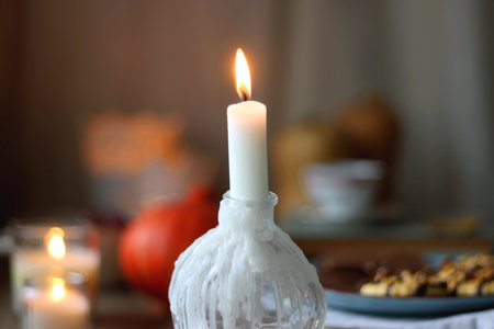 Cup of tea or coffee, plate with desserts, dried oranges, bowl of grapes, scented candles, vintage books, pumpkins and autumn leaves on the table. Autumnal hygge. Selective focus.の写真素材