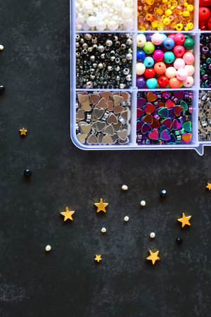 Box with colorful beads, string, wire, chain, scissors, pliers and hammer on dark background. Various jewelry making supplies. Top view.の写真素材