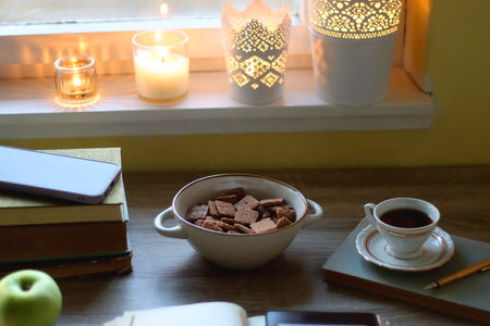 Vintage books, e-reader, pen, reading glasses, phone, cup of tea or coffee, bowl of cookies, green apple and lit candles on the table. Hygge at home, studying atmosphere.の写真素材