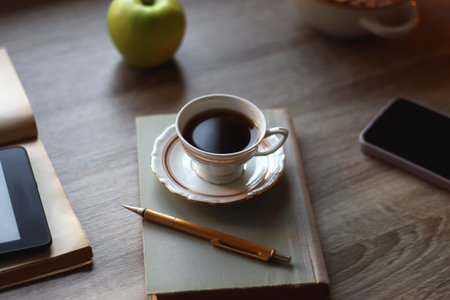 Vintage books, e-reader, pen, reading glasses, phone, cup of tea or coffee, bowl of cookies, green apple and lit candles on the table. Hygge at home, studying atmosphere.の写真素材