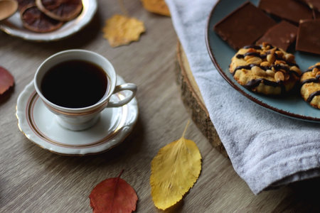 Cup of tea or coffee, plate with desserts, dried oranges, bowl of grapes, scented candles, vintage books, pumpkins and autumn leaves on the table. Autumnal hygge. Selective focus.の写真素材