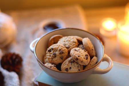Bowl of cookies, cup of tea or coffee, plate of blueberries, dry oranges, wool yarn, pine cones, books, reading glasses, tablet, pen, soft blanket and lit candles on the table.の写真素材