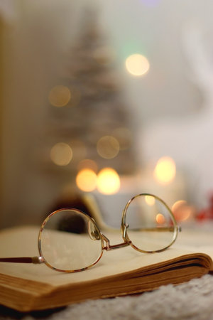 Bowl of cookies, cup of tea, dry oranges, pine cones, books, reading glasses, small presents, various Christmas decorations and lit candles on the table. Cozy Christmas hygge.の写真素材