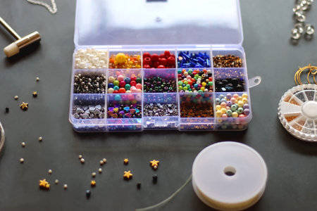 Box with colorful beads, string, wire, chain, scissors, pliers and hammer on dark background....