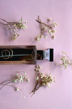 Unrecognizable perfume bottle and gypsophila flowers on pastel pink background. Flat lay.の写真素材
