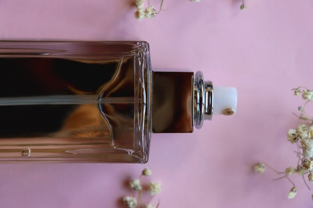 Unrecognizable perfume bottle and gypsophila flowers on pastel pink background. Flat lay.
