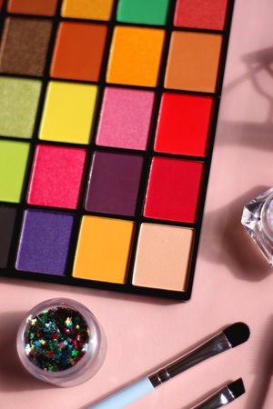Colorful eyeshadow palette, glitter, make up brushes, mascara, eyeliner, lash curler and brow gel on bright pink background. Various eye beauty products. Selective focus.の写真素材