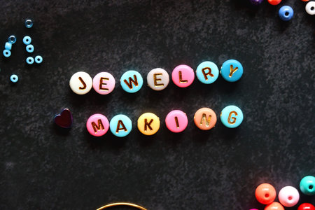 Colorful beads and various jewelry making supplies on dark background. Letter beads spelling JEWELRY...