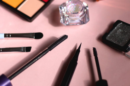 Colorful eyeshadow palette, glitter, make up brushes, mascara, eyeliner, lash curler and brow gel on bright pink background. Various eye beauty products. Selective focus.の写真素材