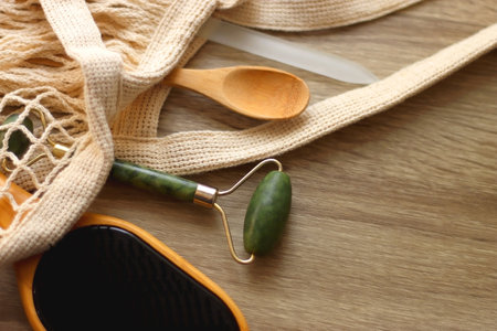 Crochet bag, wooden hairbursh, face roller, reusable razor, glass nail file, wooden toothbrush and wooden spoon on wooden background. Various zero waste products. Selective focus.の写真素材