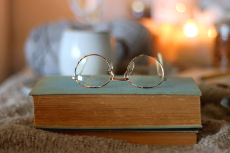 Cup of tea or coffee, cookies, books, glasses, e-reader, almonds, ball of yarn, knitting needles and lit candles on the table. Hygge at home. Selective focus.の写真素材