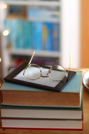 Cup of tea or coffee, pile of books, plate of cookies, reading glasses, e-reader and pen on the...