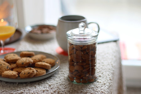 Cup of tea or coffee, stack of books, e-reader, glasses, various cookies, almonds, orange juice and lit candles on the table. Hygge at home. Selective focus.の写真素材