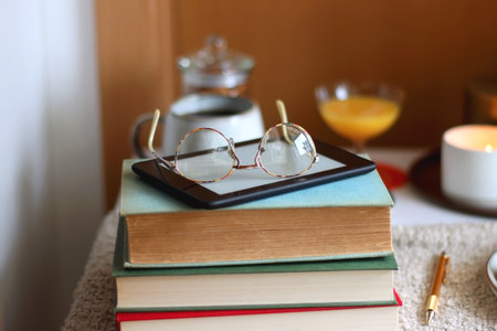 Cup of tea or coffee, stack of books, e-reader, glasses, various cookies, almonds, orange juice and lit candles on the table. Hygge at home. Selective focus.の写真素材