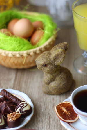 Easter eggs in the basket, bowl of cookies, chocolate pralines, Easter bunny figurine, cups of tea,...