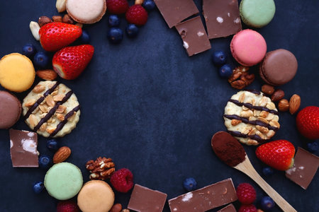 Macarons, chocolate, cookies, berries and various nuts on dark blue background. Top view.