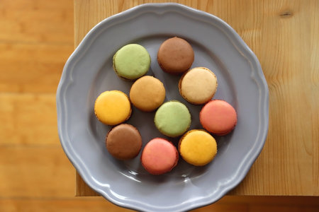 Purple plate filled with pastel macarons on wooden table. Top view.の写真素材