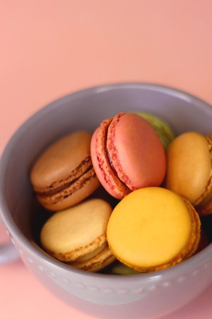 Purple cup filled with pastel macarons on pink background. Selective focus.の写真素材