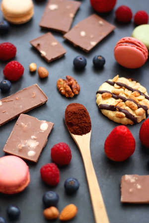 Macarons, chocolate, cookies, berries and various nuts on dark blue background. Selective focus.