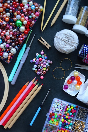 Colorful beads, coloring pencils, glitter, needles, string, hoop, tape and scissors on dark background. Various colorful craft supplies. Flat lay.の写真素材