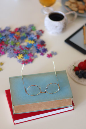Colorful jigsaw puzzle pieces, books, tablet, glasses, cookies, berries, cup of tea or coffee, glass...