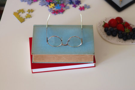 Colorful jigsaw puzzle pieces, books, tablet, glasses, cookies, berries, cup of tea or coffee, glass of juice and lit candles on the table. Hygge in pastel colors. Selective focus.の写真素材