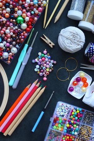 Colorful beads, coloring pencils, glitter, needles, string, hoop, tape and scissors on dark...