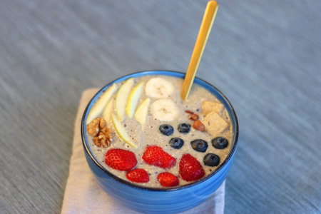 Bowl filled with healthy smoothie, fruit pieces and nuts on the table. Selective focus.の写真素材