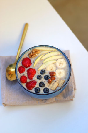 Bowl filled with healthy smoothie, fruit pieces and nuts on the table. Selective focus.の写真素材