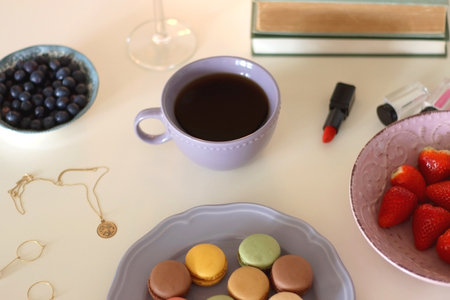 Plate of pastel macarons, cookies and chocolate, cup of tea of coffee, glass of bubble water, various berries, books and accessories on the table. Selective focus, pastel colors.の写真素材