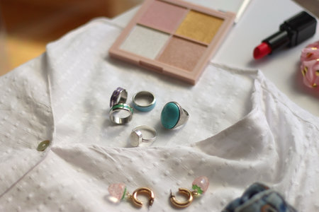 White blouse, denim skirt, colorful rings, earrings and beauty products on white background. Summer outfit in pastel colors. Selective focus.の写真素材
