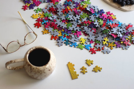 Colorful jigsaw puzzle pieces, books, tablet, glasses, cookies, berries, cup of tea or coffee, glass of juice and lit candles on the table. Hygge in pastel colors. Selective focus.の写真素材