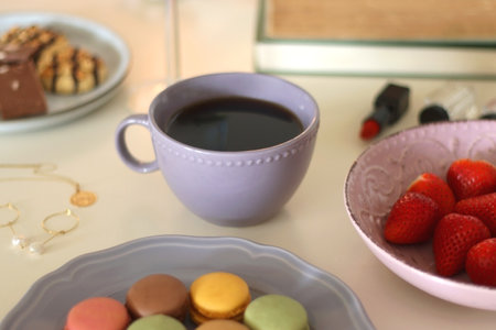 Plate of pastel macarons, cookies and chocolate, cup of tea of coffee, glass of bubble water, various berries, books and accessories on the table. Selective focus, pastel colors.の写真素材
