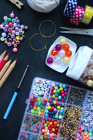 Colorful beads, coloring pencils, glitter, needles, string, hoop, tape and scissors on dark...