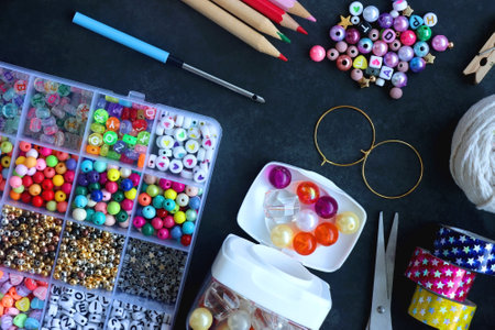 Colorful beads, coloring pencils, glitter, needles, string, hoop, tape and scissors on dark background. Various colorful craft supplies. Flat lay.の写真素材