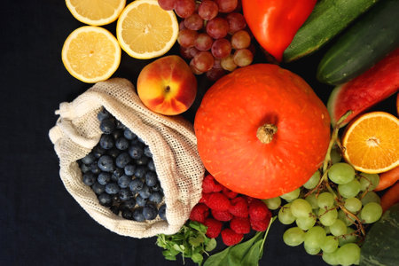 Round straw bag and variosu seasonal fruits and vegetables on dark background. Summer and fall produce. Top view.の写真素材