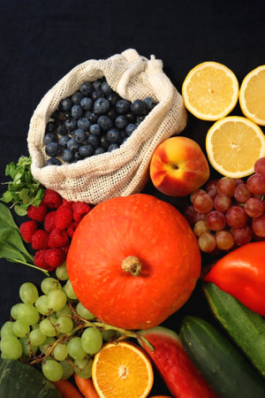 Round straw bag and variosu seasonal fruits and vegetables on dark background. Summer and fall produce. Top view.の写真素材
