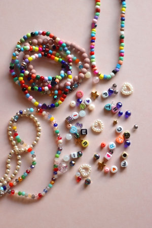 Colorful DIY necklaces, friendship bracelets and various plastic beads on pastel pink background. Flat lay.の写真素材