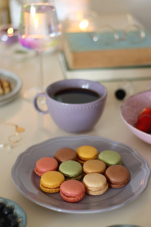 Plate of pastel macarons, cookies and chocolate, cup of tea of coffee, glass of bubble water, various berries, books and accessories on the table. Selective focus, pastel colors.の写真素材