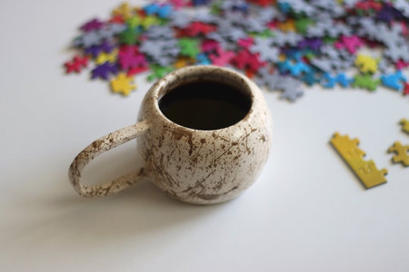 Colorful jigsaw puzzle pieces, cup of tea or coffee, eyeglasses and fresh berries for snacking. Hygge at home. Selective focus.の写真素材