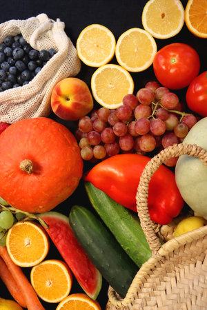 Round straw bag and various seasonal fruits and vegetables on dark background. Summer and fall produce. Top view.の写真素材