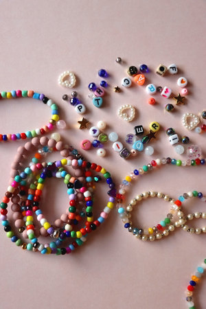 Colorful DIY necklaces, friendship bracelets and various plastic beads on pastel pink background. Flat lay.の写真素材