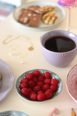 Plate of pastel macarons, cookies and chocolate, cup of tea of coffee, glass of bubble water, various berries, books and accessories on the table. Selective focus, pastel colors.の写真素材