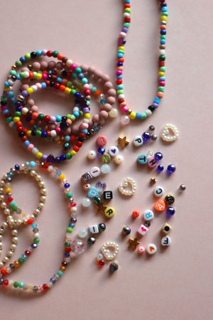 Colorful DIY necklaces, friendship bracelets and various plastic beads on pastel pink background. Flat lay.の写真素材